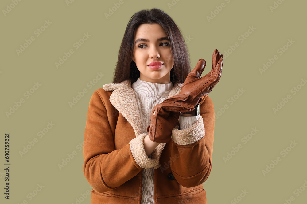 Stylish young woman in leather gloves on green background