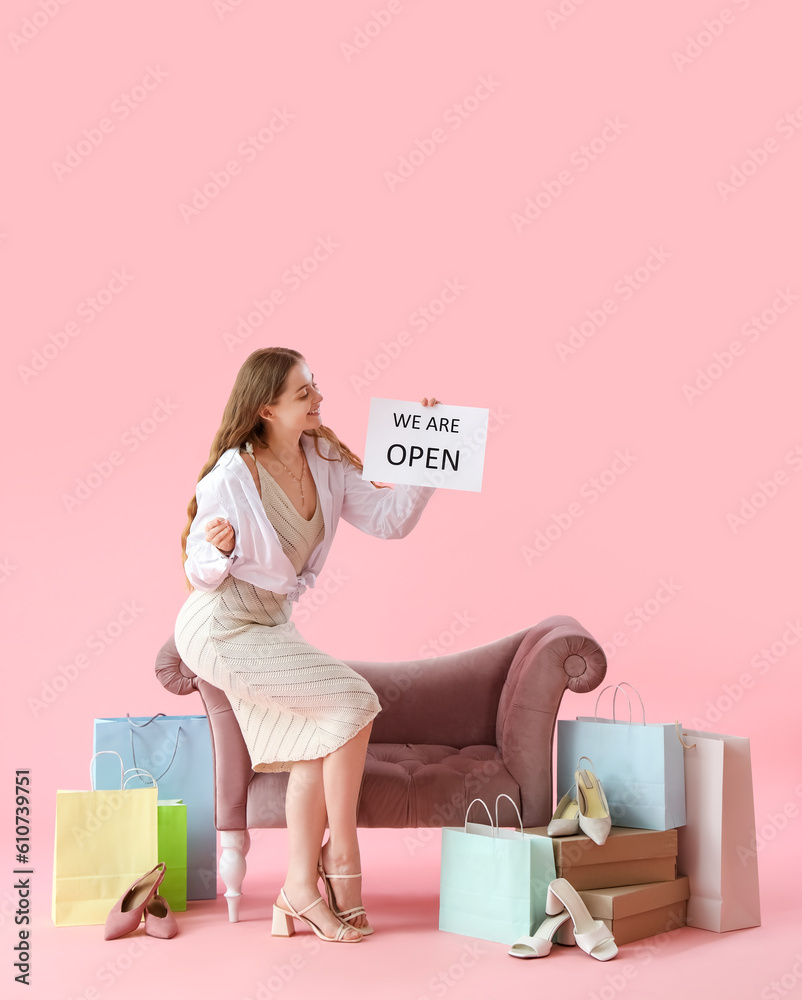Young woman with opening sign, shoes and shopping bags on pink background