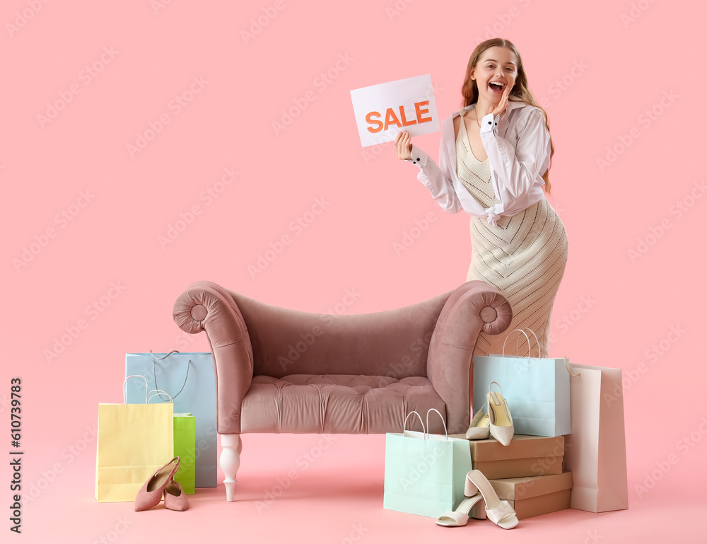 Young woman with sale sign, shoes and shopping bags on pink background