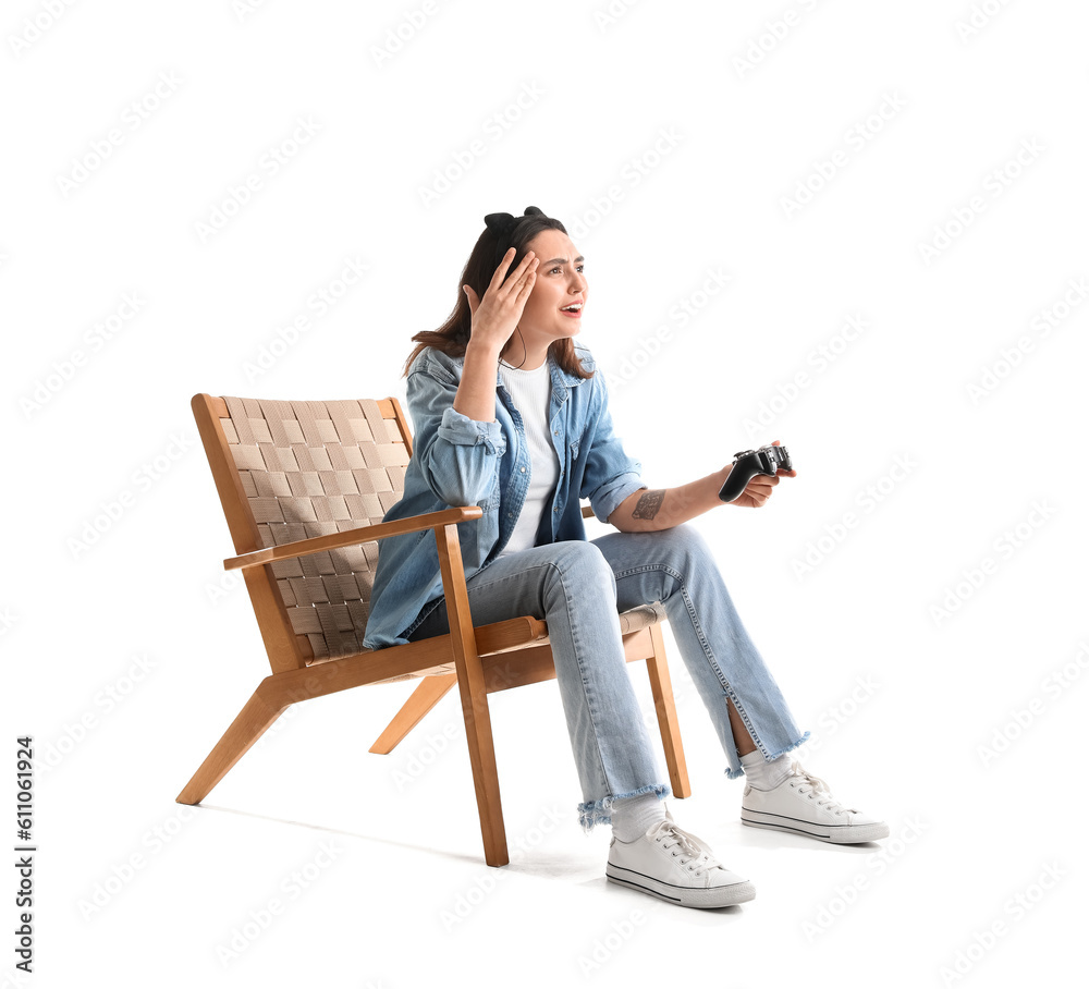 Young woman with headphones playing video game in wooden armchair on white background