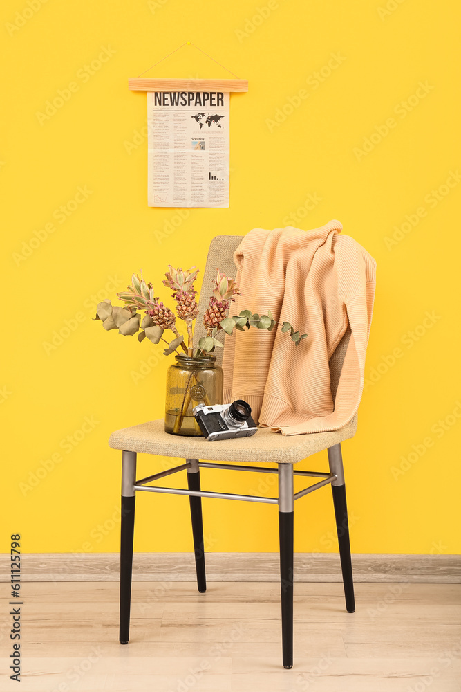 Vase with baby pineapples, eucalyptus and photo camera on chair near yellow wall
