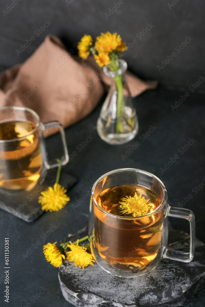 Board with glass cups of healthy dandelion tea on black table