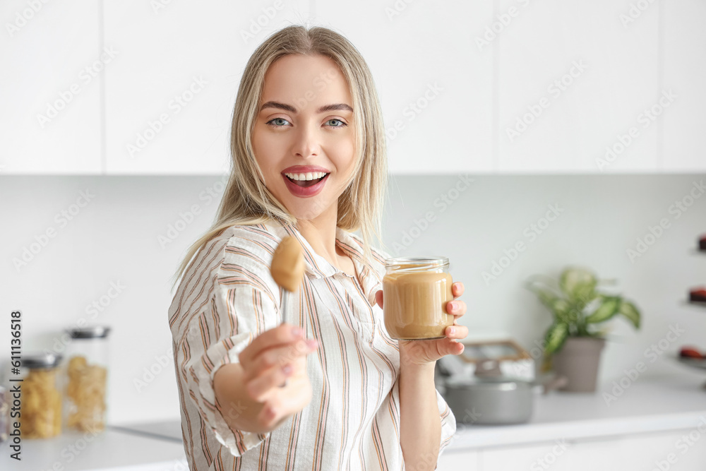Young woman with spoon and jar of nut butter in kitchen