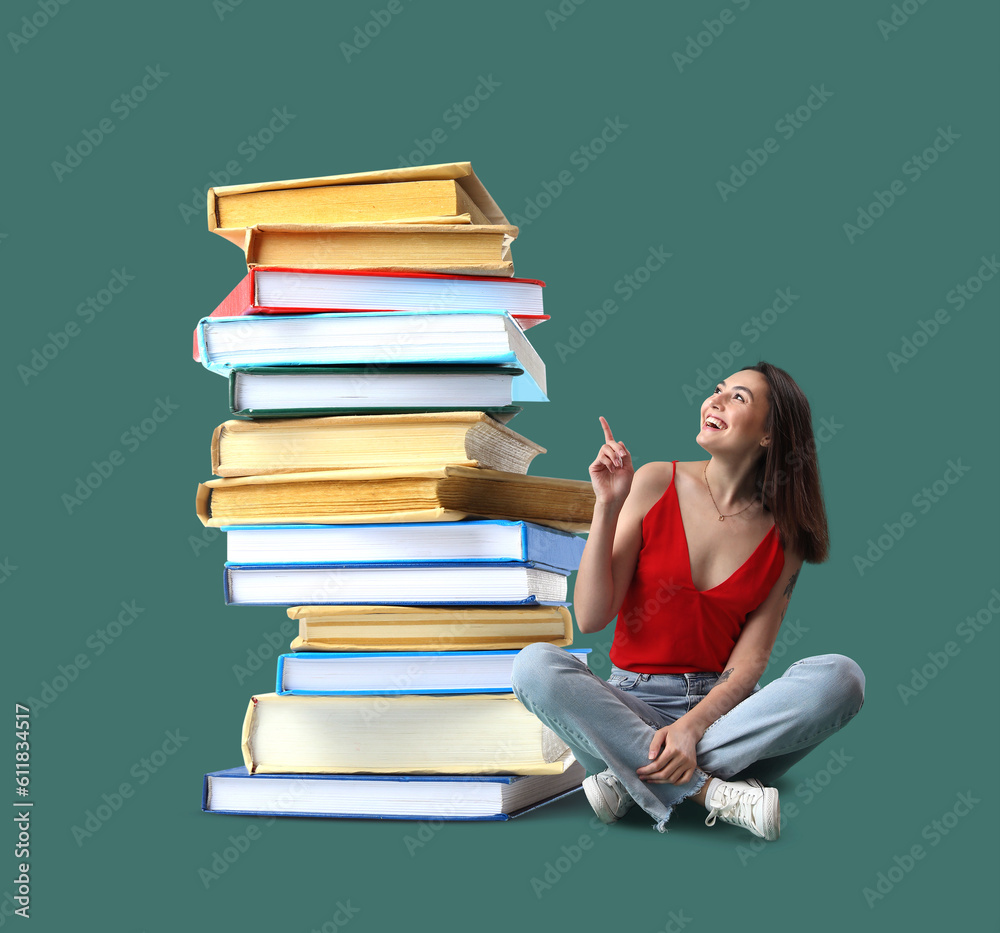 Happy young woman sitting near stack of big books against green background