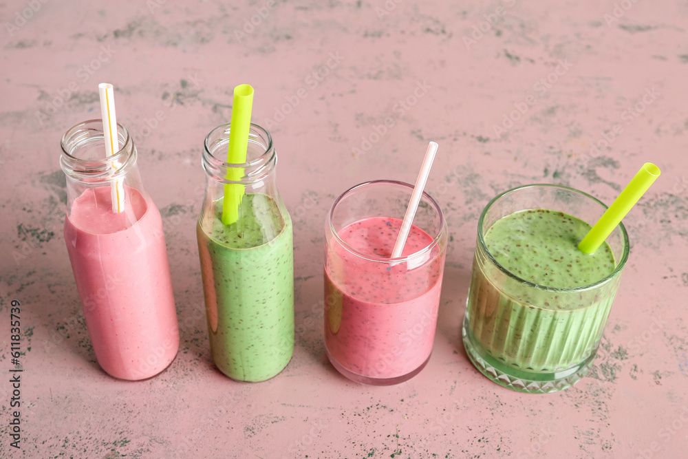 Glasses and bottles of colorful smoothie on pink background