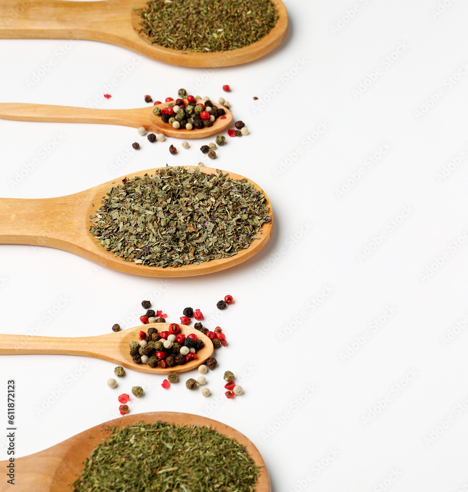 Wooden spoons with dried herbs and peppercorns on light background, closeup