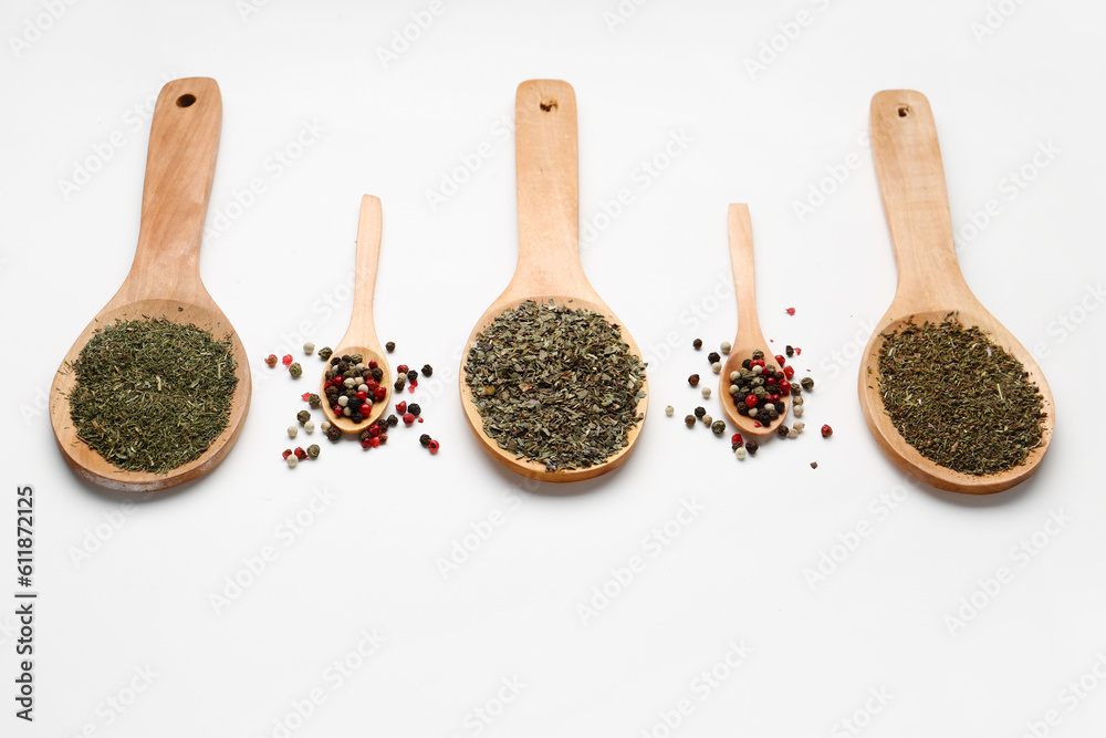 Wooden spoons with dried herbs and peppercorns on light background