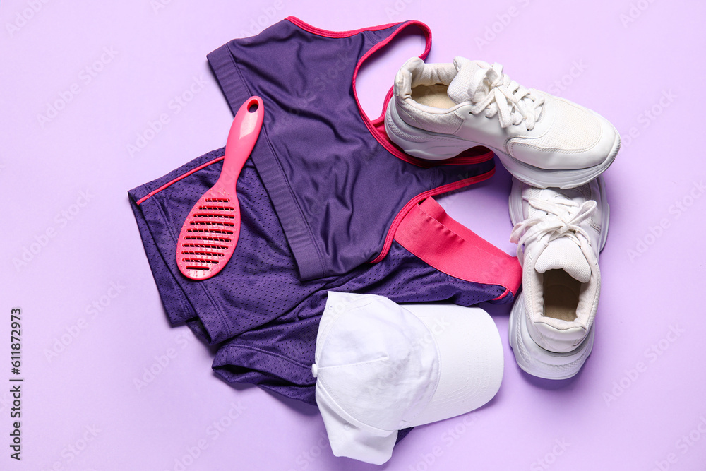 Stylish female sportswear, shoes, cap and hair brush on lilac background