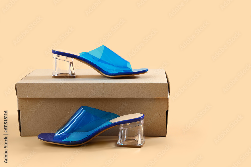 Cardboard box with blue heeled shoes on beige background