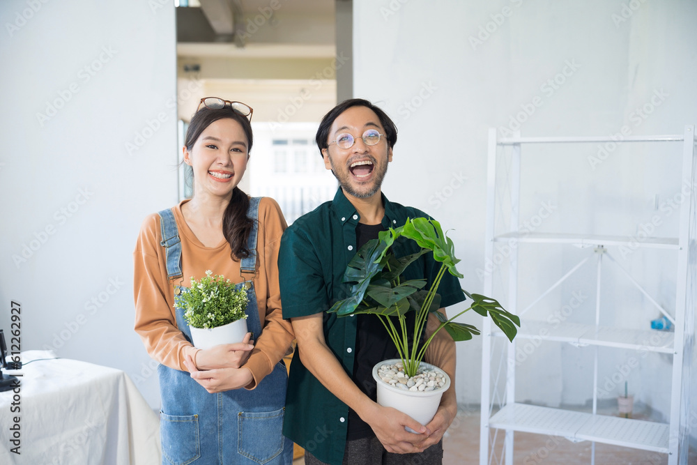 Portrait young couple moving to new house holding Flower Pots Plant Pots looking at camera at home