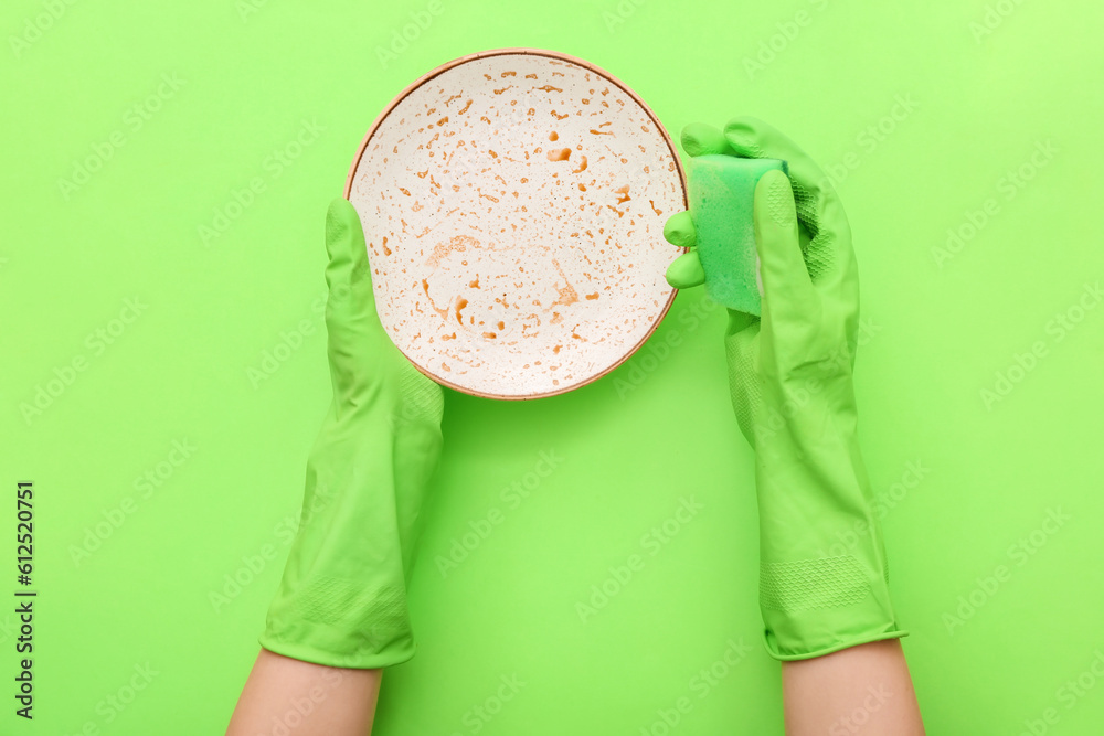 Female hands in rubber gloves washing dirty plate with sponge on green background