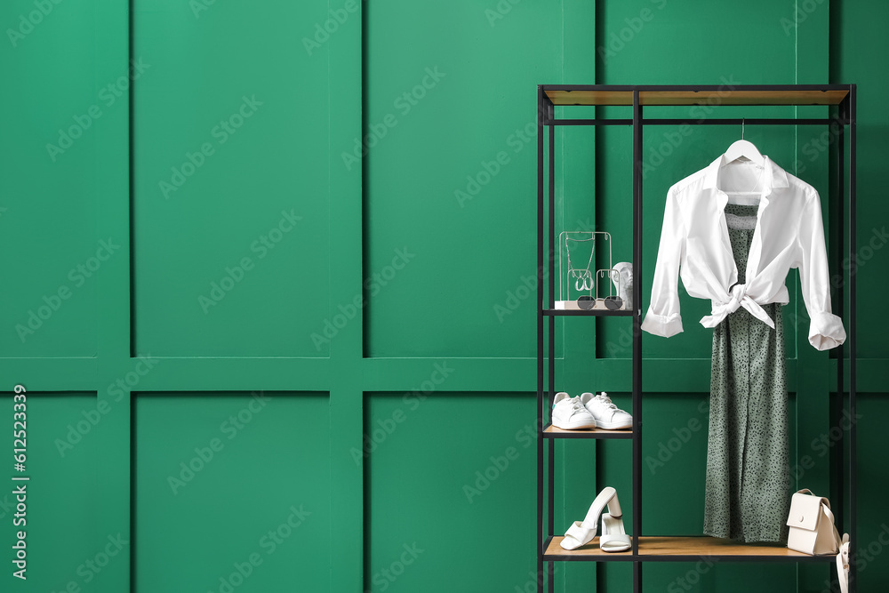 Shelving unit with clothes, shoes and accessories near green wall