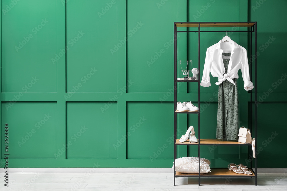 Shelving unit with clothes, shoes and accessories near green wall in room