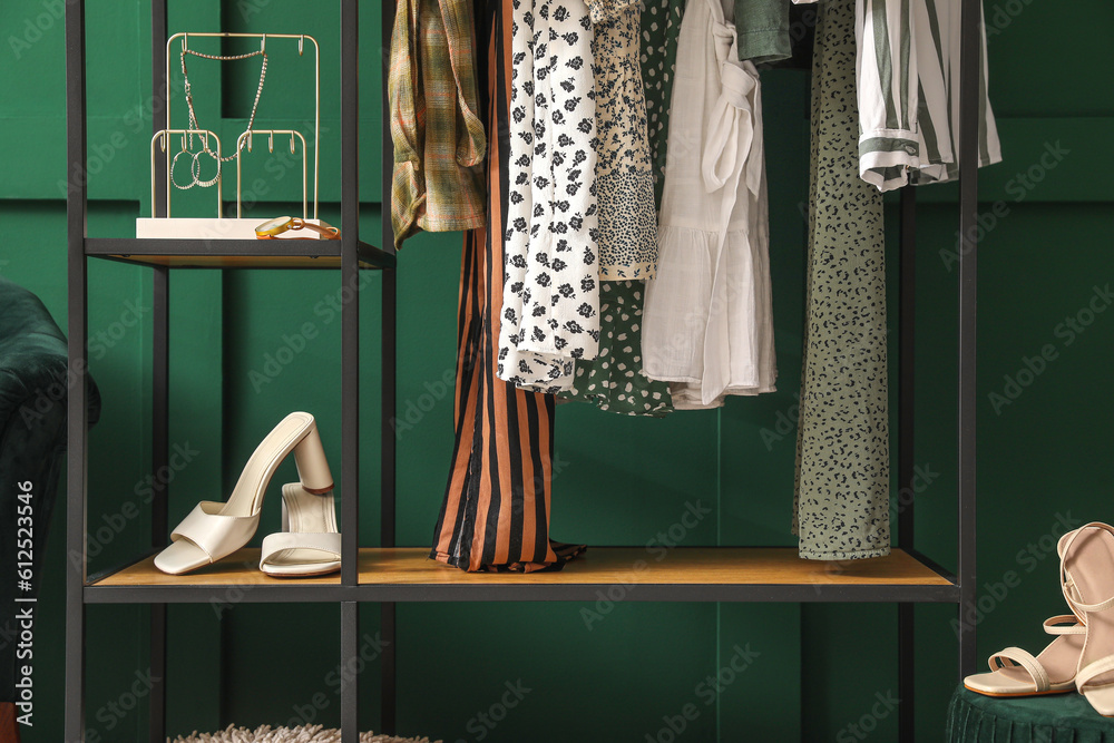 Shelving unit with clothes, shoes and accessories near green wall