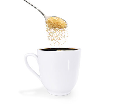 A spoonful of granulated sugar is poured into a white coffee mug. isolated on white background