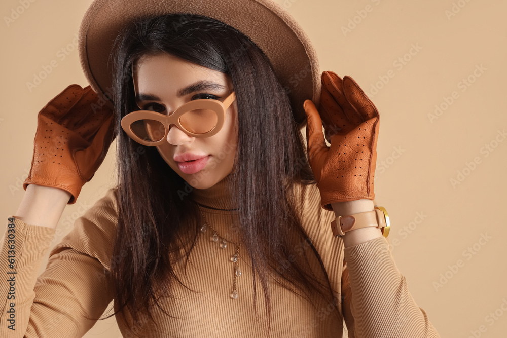 Stylish young woman in sunglasses and leather gloves on beige background