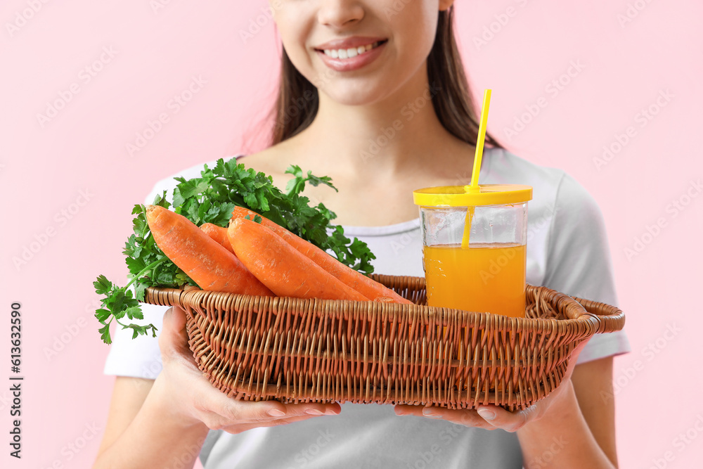 Young woman with glass of vegetable juice and carrots on pink background, closeup