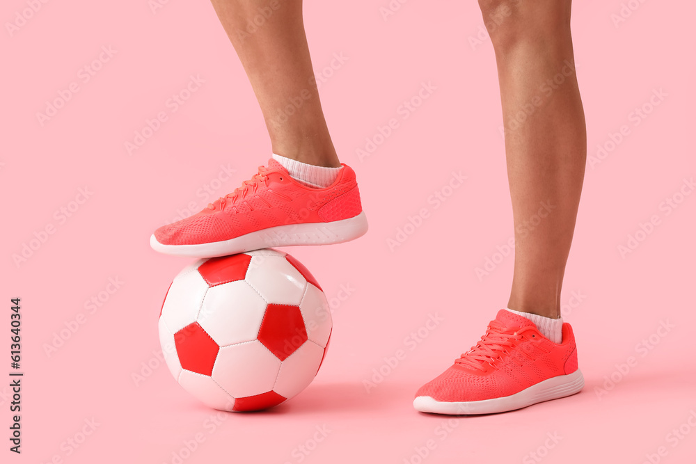 Legs of woman with soccer ball on pink background