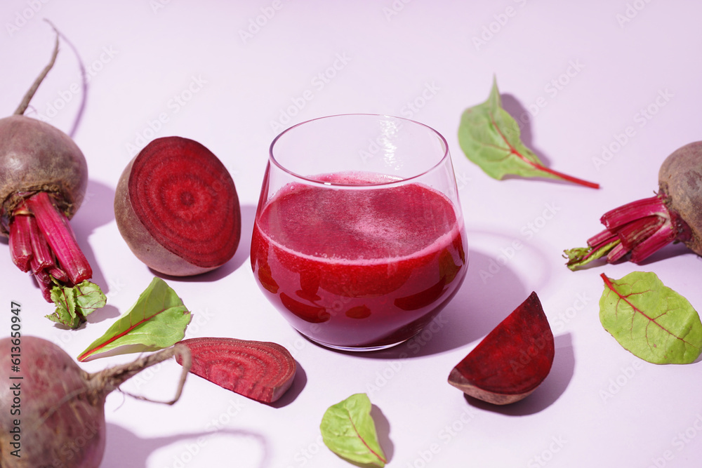 Glass of healthy beet juice and spinach on lilac background