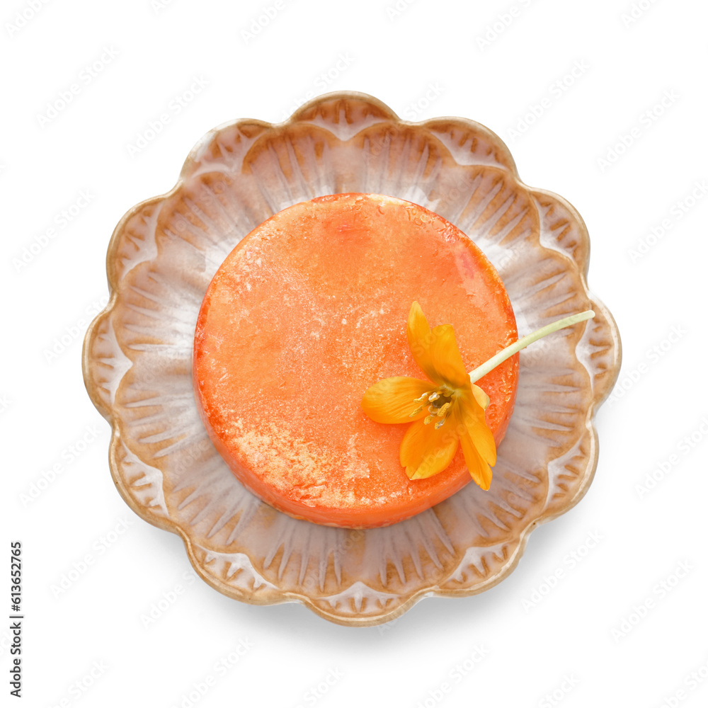 Plate with orange solid shampoo bar and flower on white background