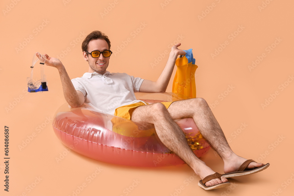 Young man with snorkeling mask, flippers and inflatable ring lying on beige background