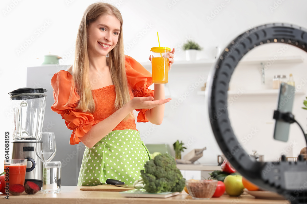 Female blogger with glass of vegetable juice recording cooking video in kitchen