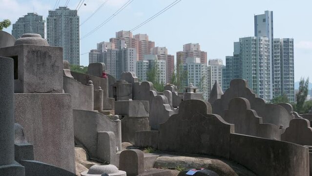 View of a tombstones at a crowded cemetery as residential buildings are seen in the background.