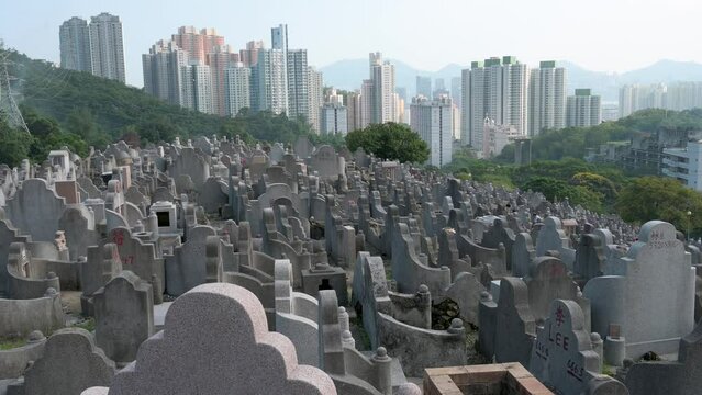 View of a gravesite at a crowded cemetery as residential buildings are seen in the background.