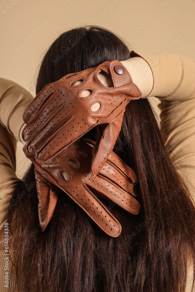 Stylish young woman in leather gloves on beige background, back view