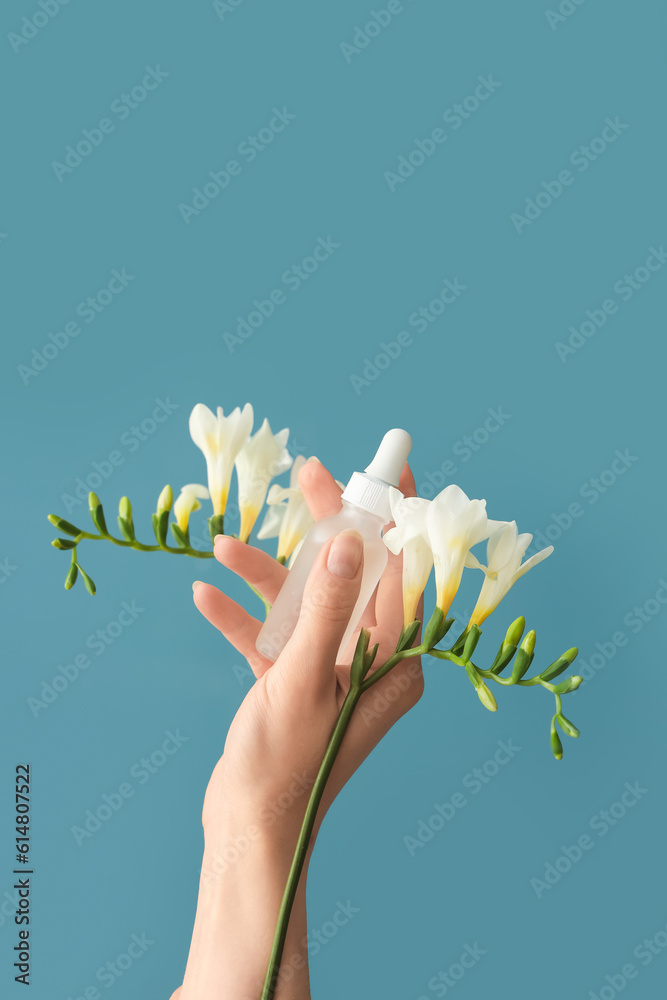 Hand holding bottle with cosmetic serum and flowers on blue background