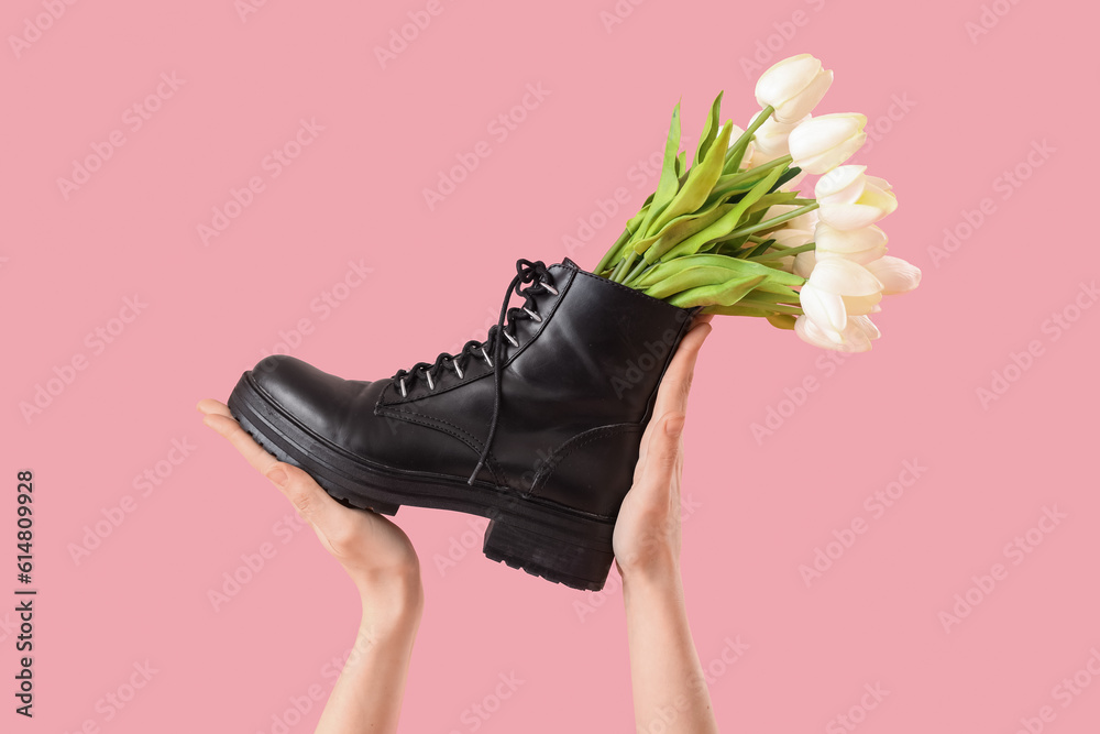 Female hands with tulip flowers in shoes on pink background