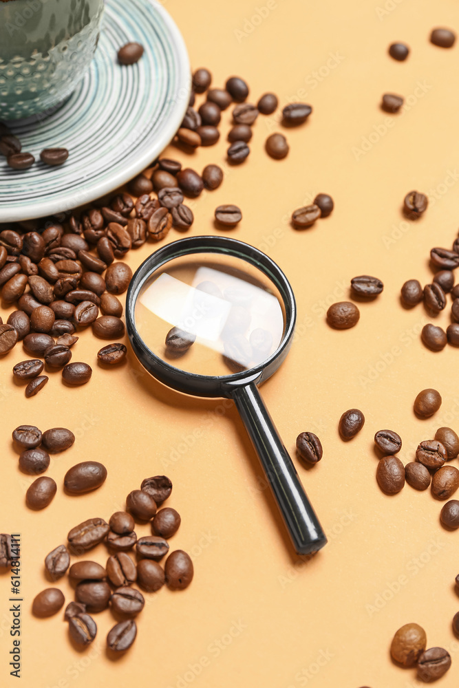 Magnifier and cup of coffee with beans on pale orange background