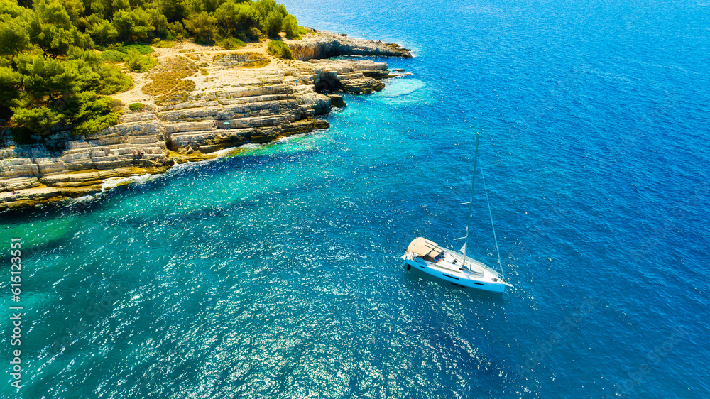 Aerial view on sail yacht, rocks and forest. Sea coastline. Vacation and adventure. Rocks and turquo