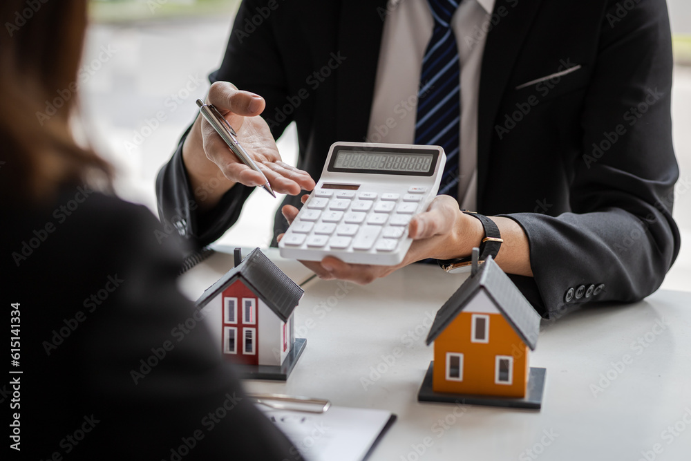 Businessman, real estate agent holding a calculator, presenting a price quote to a client for a hous