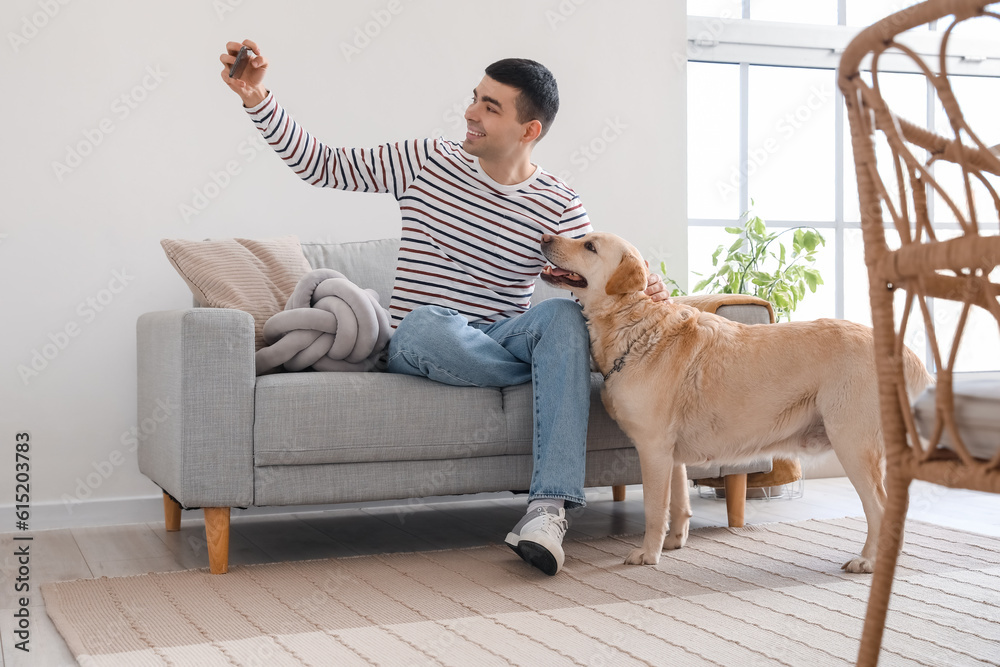 Young man with cute Labrador dog taking selfie at home