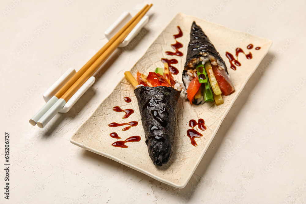 Plate with tasty sushi cones with sauce and chopsticks on light background