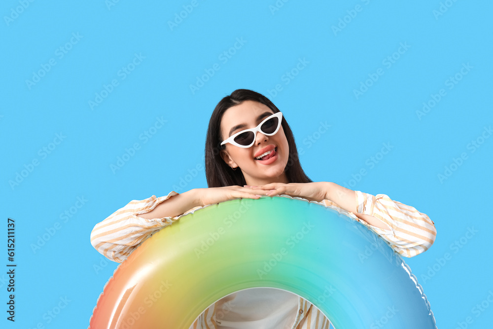 Young woman in sunglasses with inflatable ring on blue background