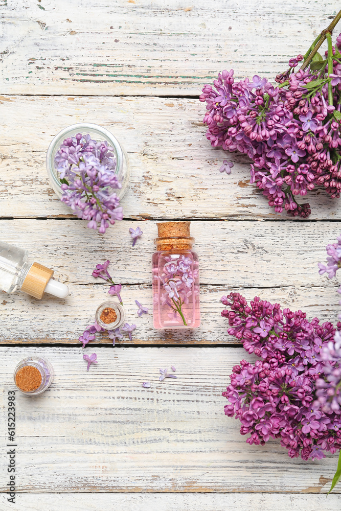 Composition with bottles of lilac essential oil and flowers on light wooden background