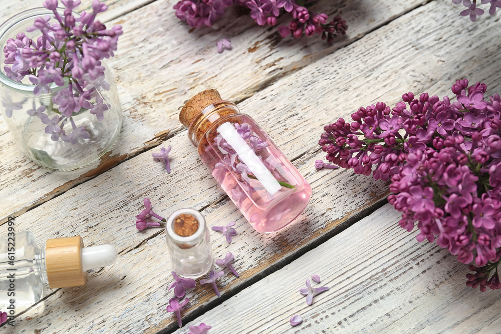 Composition with bottles of lilac essential oil and flowers on light wooden background, closeup