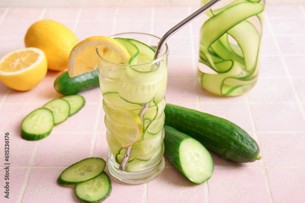 Glass and bottle of infused water with cucumber slices on pink tile table