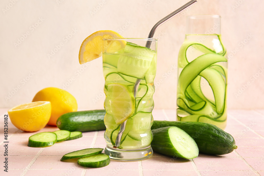 Glass and bottle of infused water with cucumber slices on pink tile table