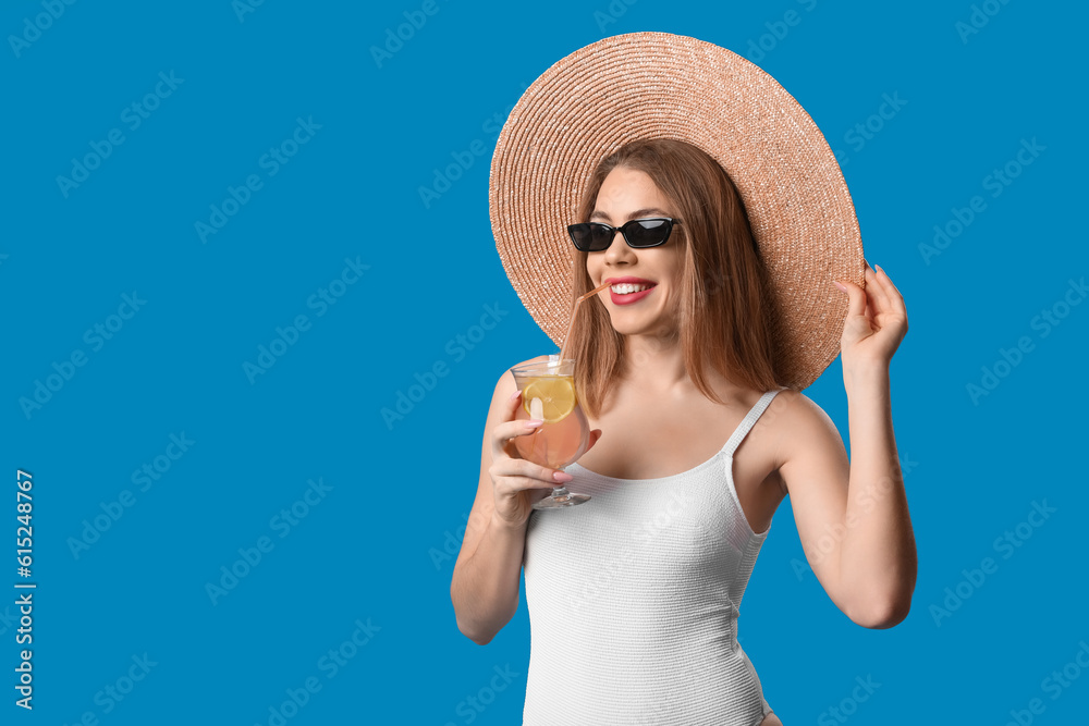 Young woman in swimsuit drinking cocktail on blue background