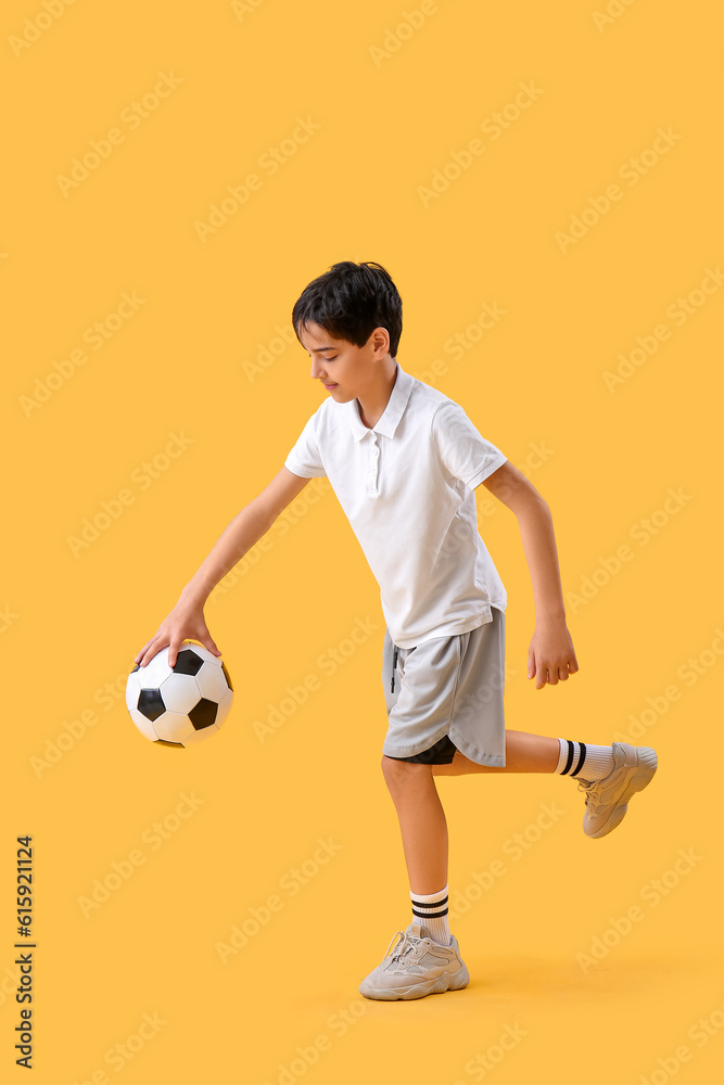 Little boy playing with soccer ball on yellow background