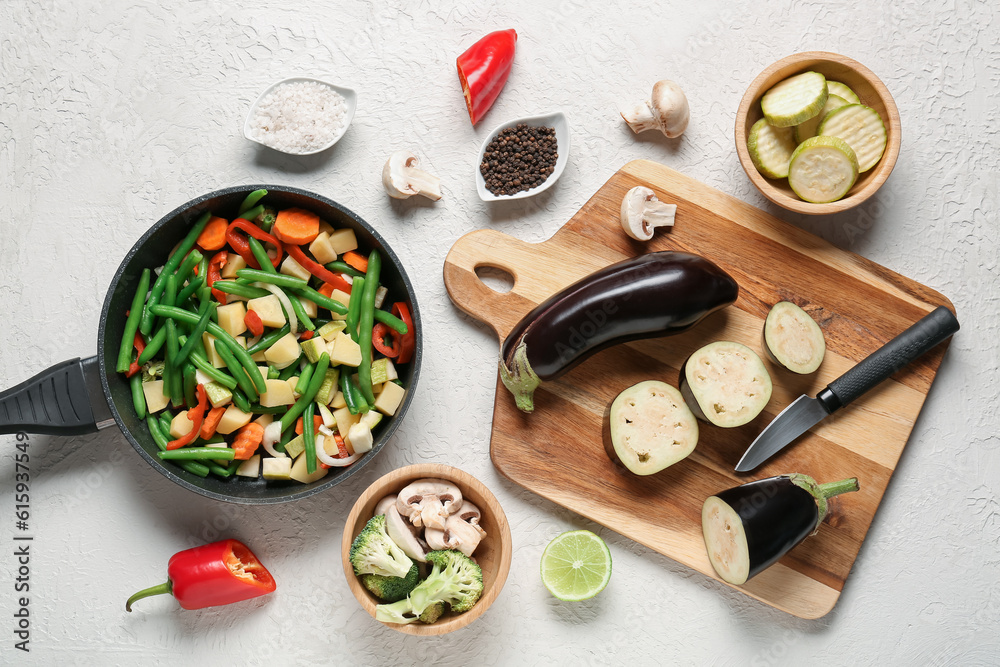 Frying pan and wooden board with fresh vegetables on light background
