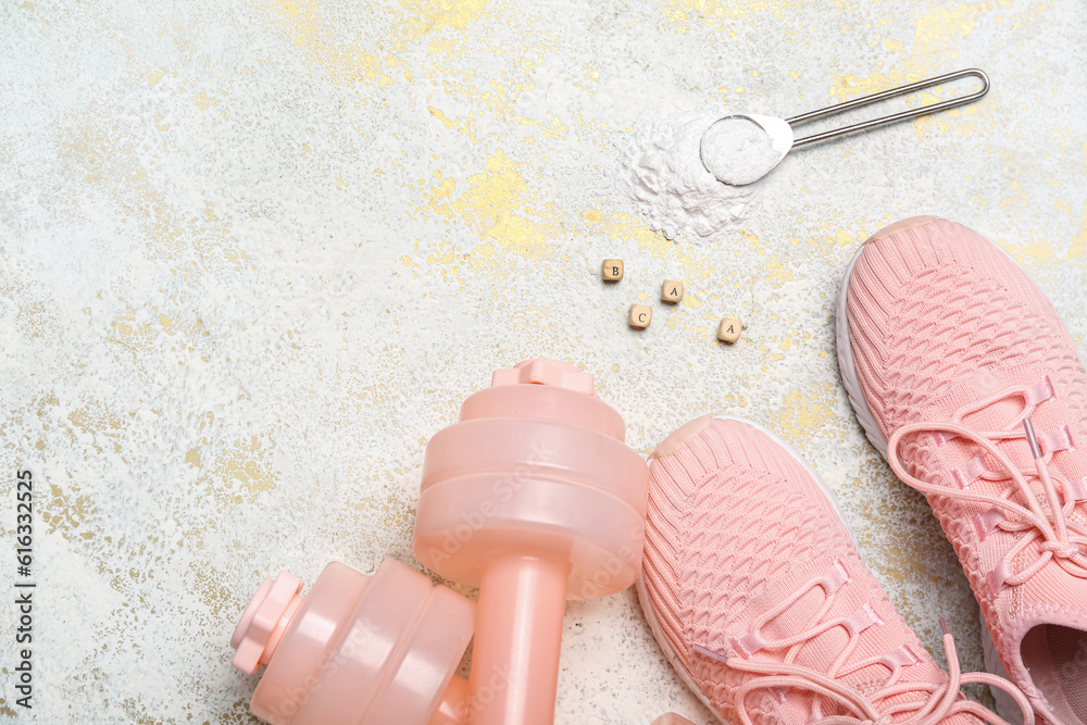 Dumbbells, shoes and scoop of amino acid supplement on light background