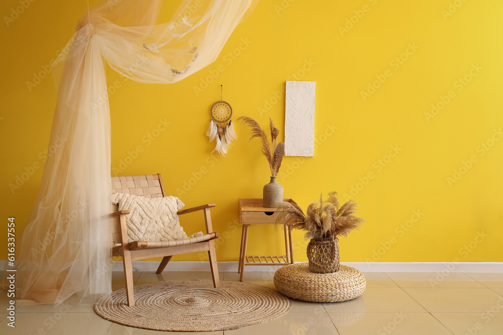 Interior of modern living room with armchair, table and dream catcher hanging on yellow wall