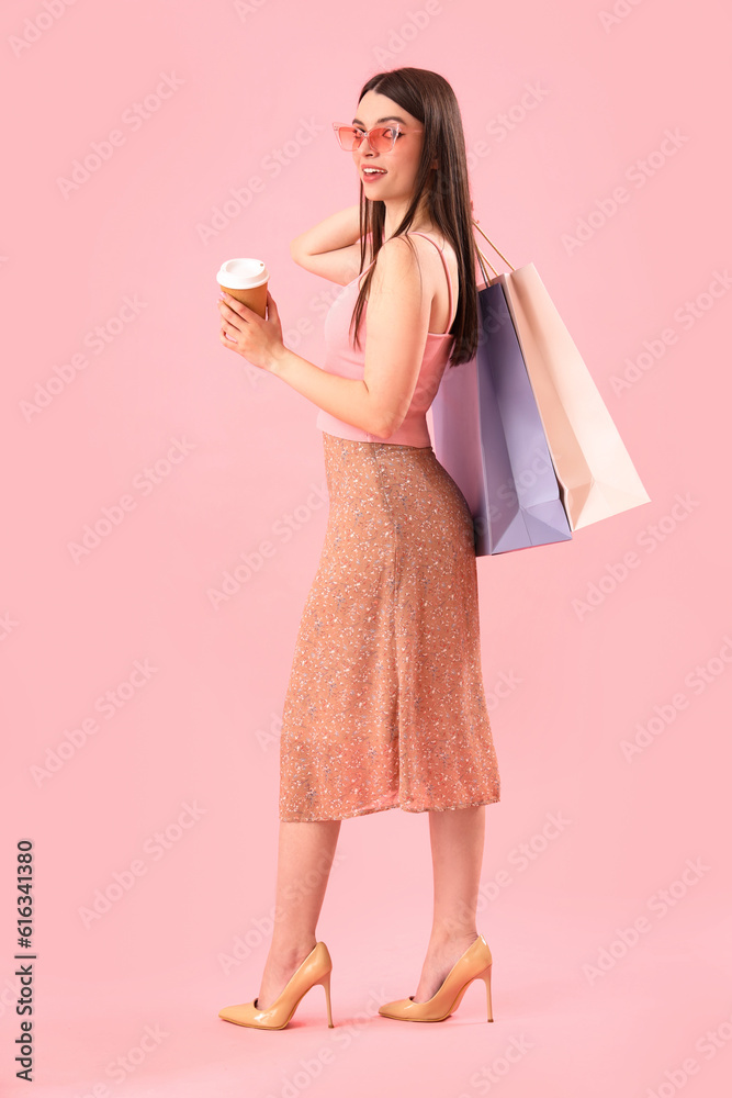 Young woman with shopping bags and cup of coffee on pink background