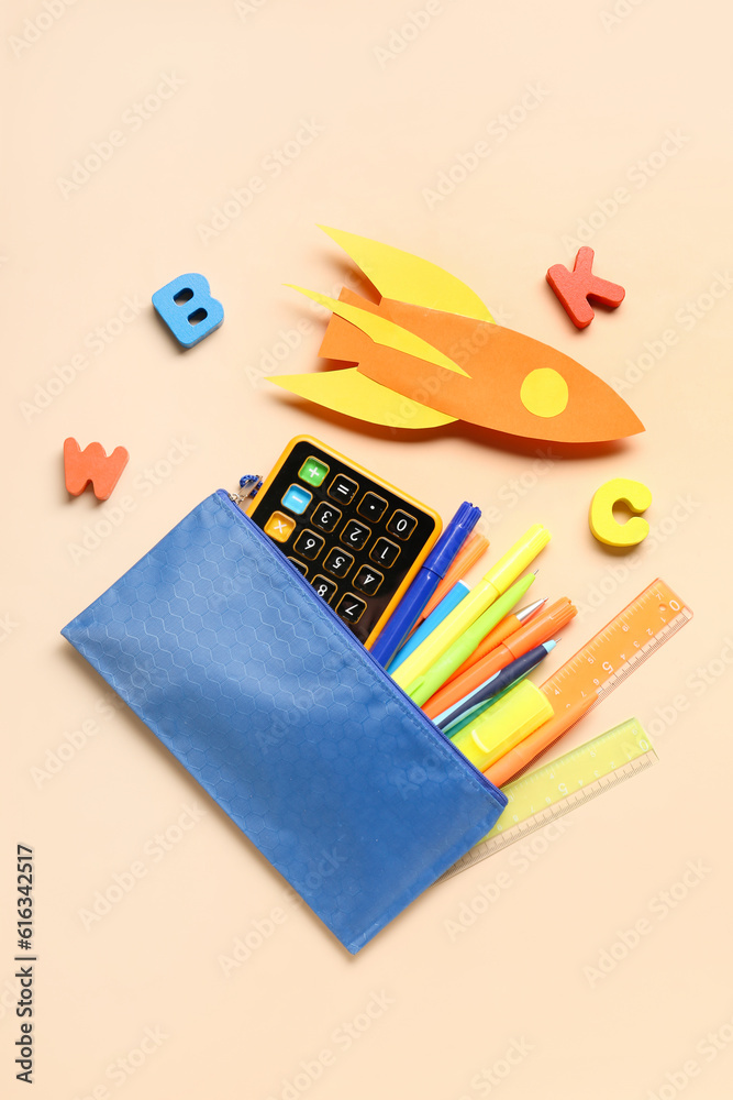 Paper rocket with calculator, pencil case and wooden letters on beige background