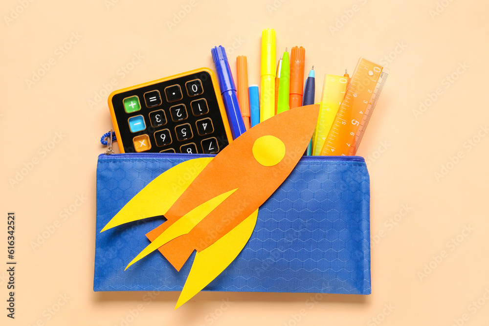 Paper rocket with calculator, pencil case and markers on beige background