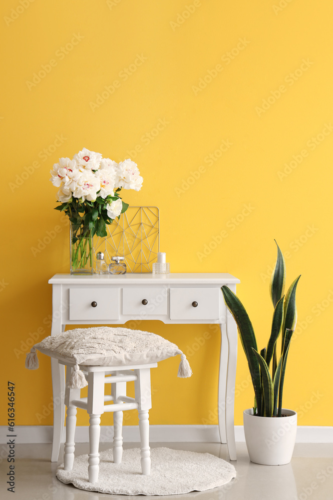 Vase of white peonies with dressing table, chair and houseplant near yellow wall